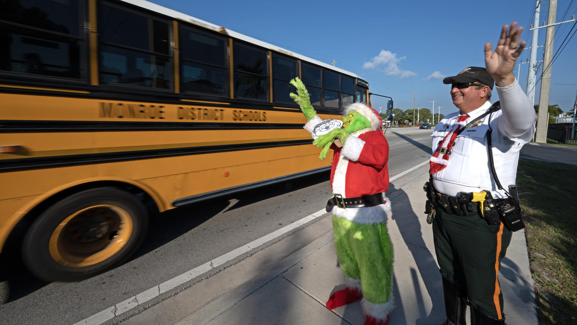 Fotografía cedida por la Oficina de noticias de los Cayos de Florida donde aparece el coronel de la oficina del alguacil del condado de Monroe, Lou Caputo, disfrazado de Grinch, y el diputado Andrew Leird (d), mientras saludan a un autobús escolar que circula por la autopista Florida Keys Overseas hoy, en Marathon, Florida (Estados Unidos). EFE/ Andy Newman /Florida Keys News Bureau/ SOLO USO EDITORIAL/ SOLO DISPONIBLE PARA ILUSTRAR LA NOTICIA QUE ACOMPAÑA (CRÉDITO OBLIGATORIO)
