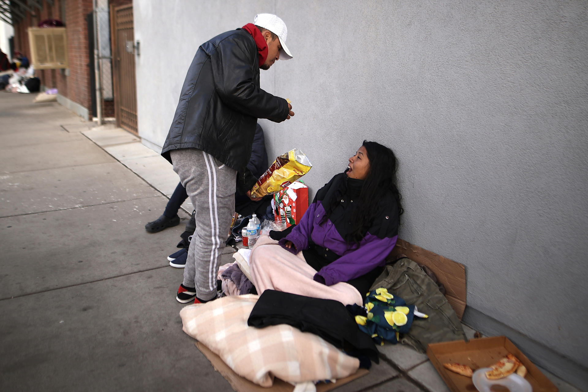 Unos inmigrantes indocumentados que recién cruzaron la frontera desde México comen en el suelo donde duermen el martes 13 de diciembre en una calle de la ciudad fronteriza de El Paso, Texas. EFE/Jesús Rosales
