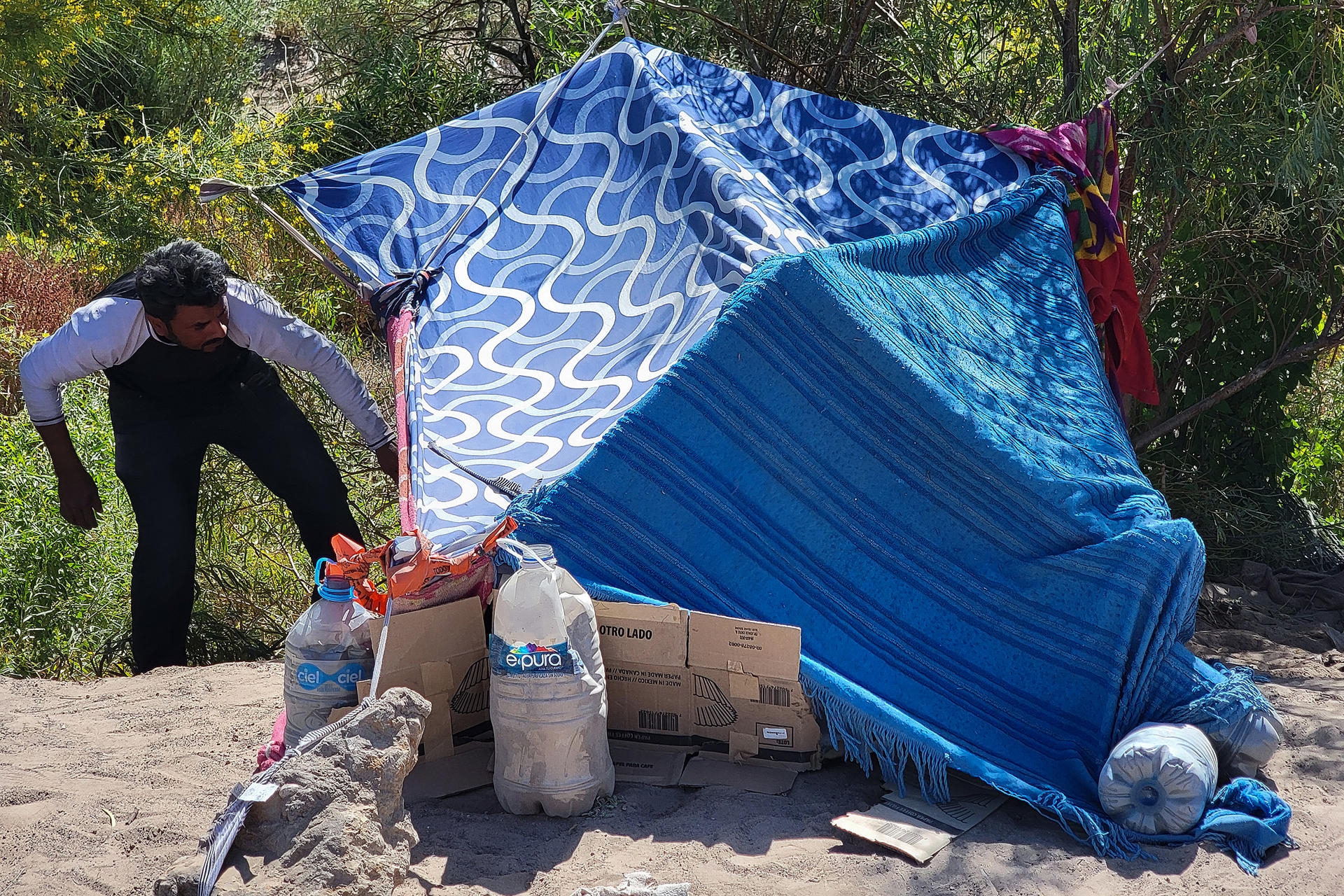 Un migrante organiza una carpa hecha por cobijas a orillas del Río Bravo, el 1 de julio de 2024 en Ciudad Juárez (México). EFE/ Luis Torres
