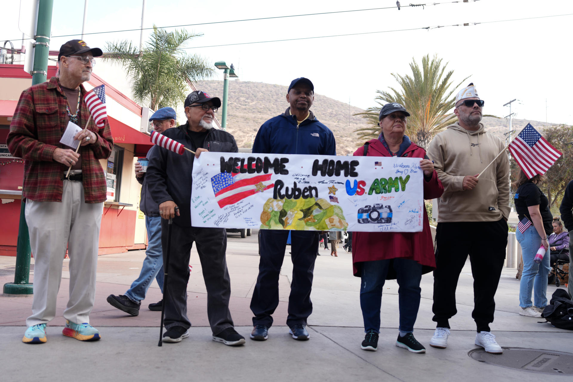 Un grupo de veteranos sostienen una pancarta de bienvenida mientras esperan al veterano de las fuerzas militares estadounidenses Rubén Robles este jueves, en la frontera de San Ysidro en San Diego, California (Estados Unidos). EFE/ Manuel Ocaño
